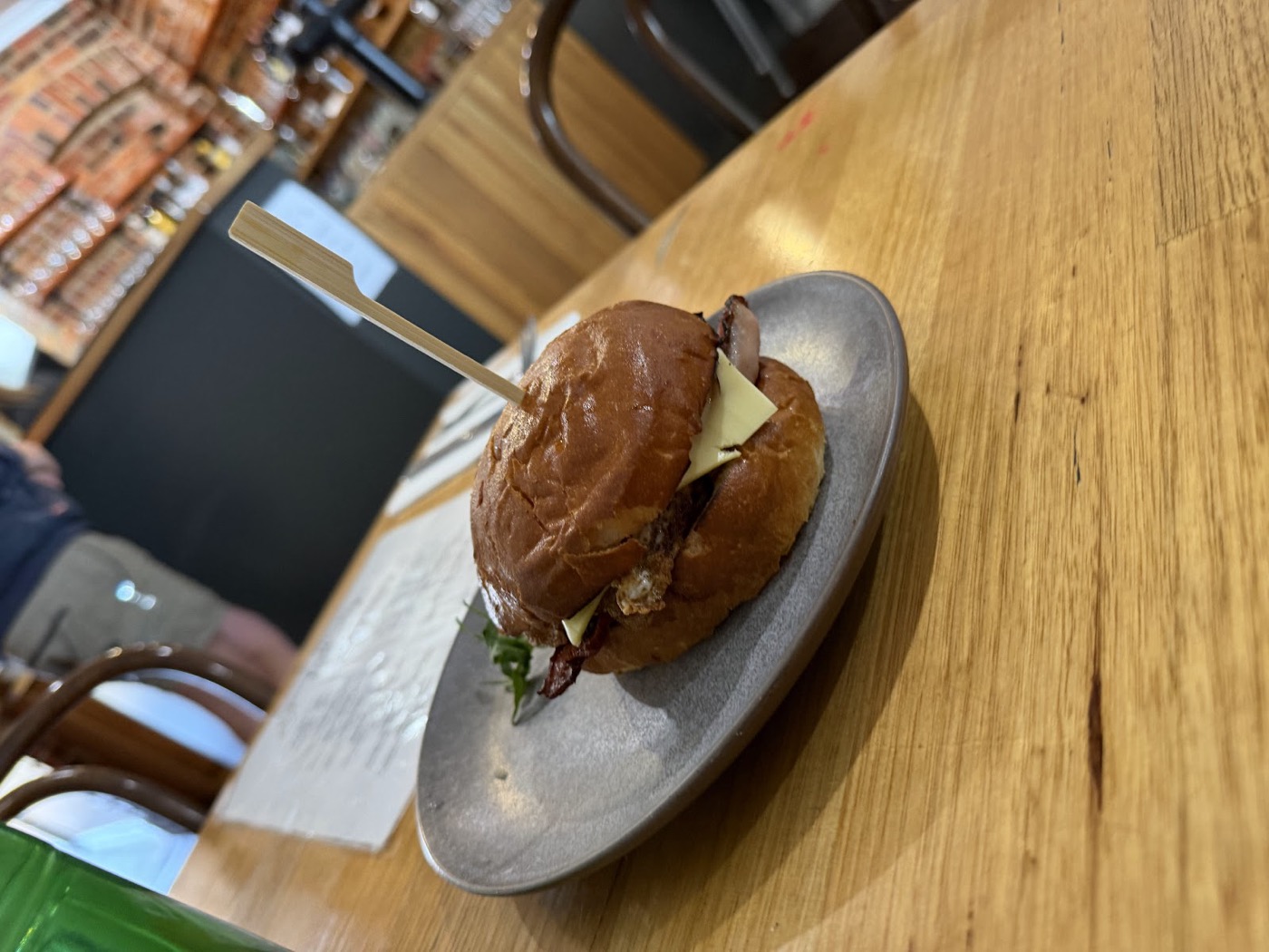 A toasted bun held together with a wooden pick, on a grey plate on a timber table