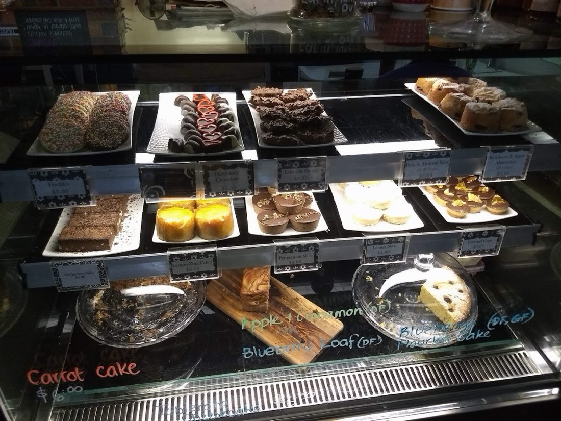 The cabinet full of cakes and slices on trays, with chalk labels below for carrot cake, apple and cinnamon and blueberry loaf