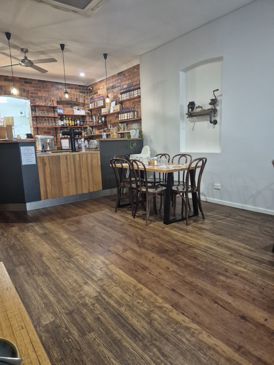 The dining room: a timber floor, café tables with bentwood chairs, a timber-fronted counter and a brick wall of shelves behind it