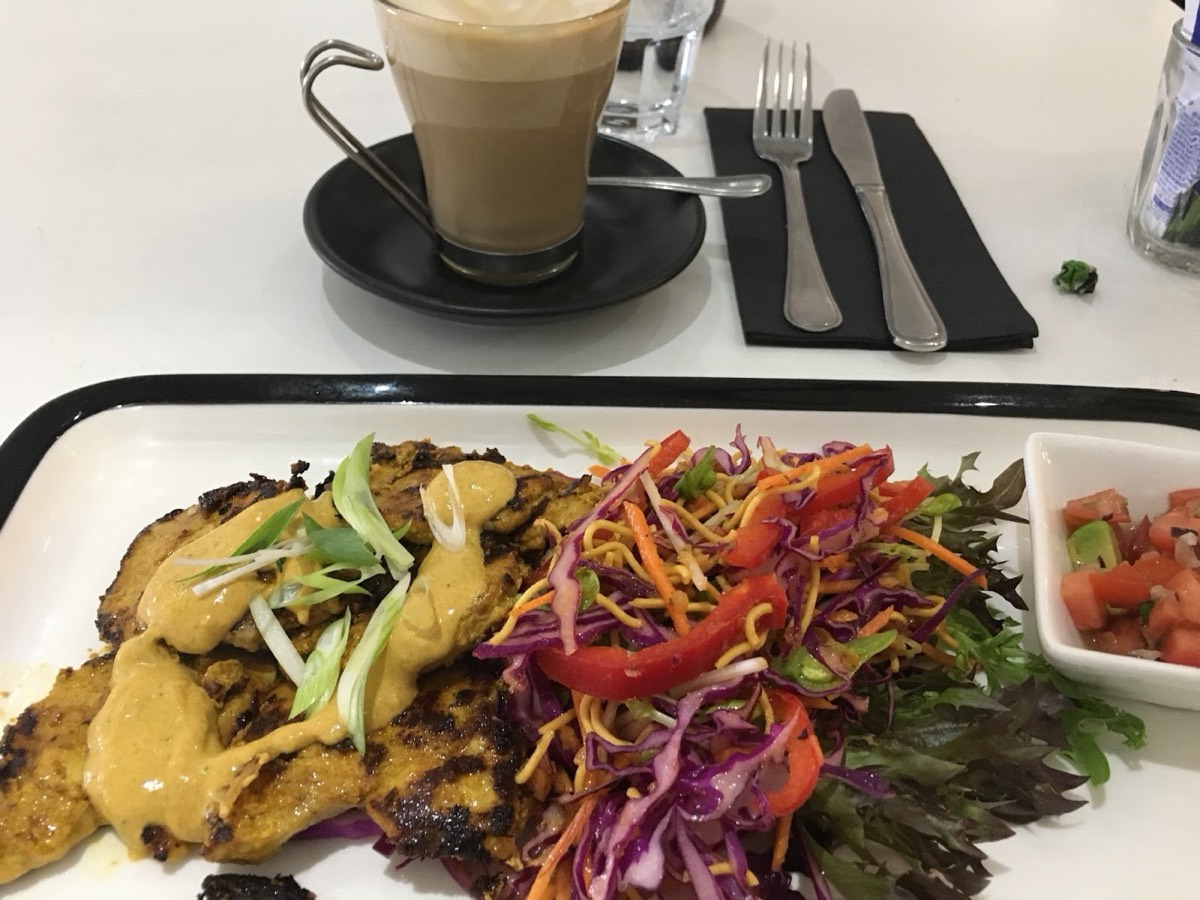 Golden patties with a yellow sauce and spring onion on a colourful salad of red cabbage, carrot and capsicum, beside a latte